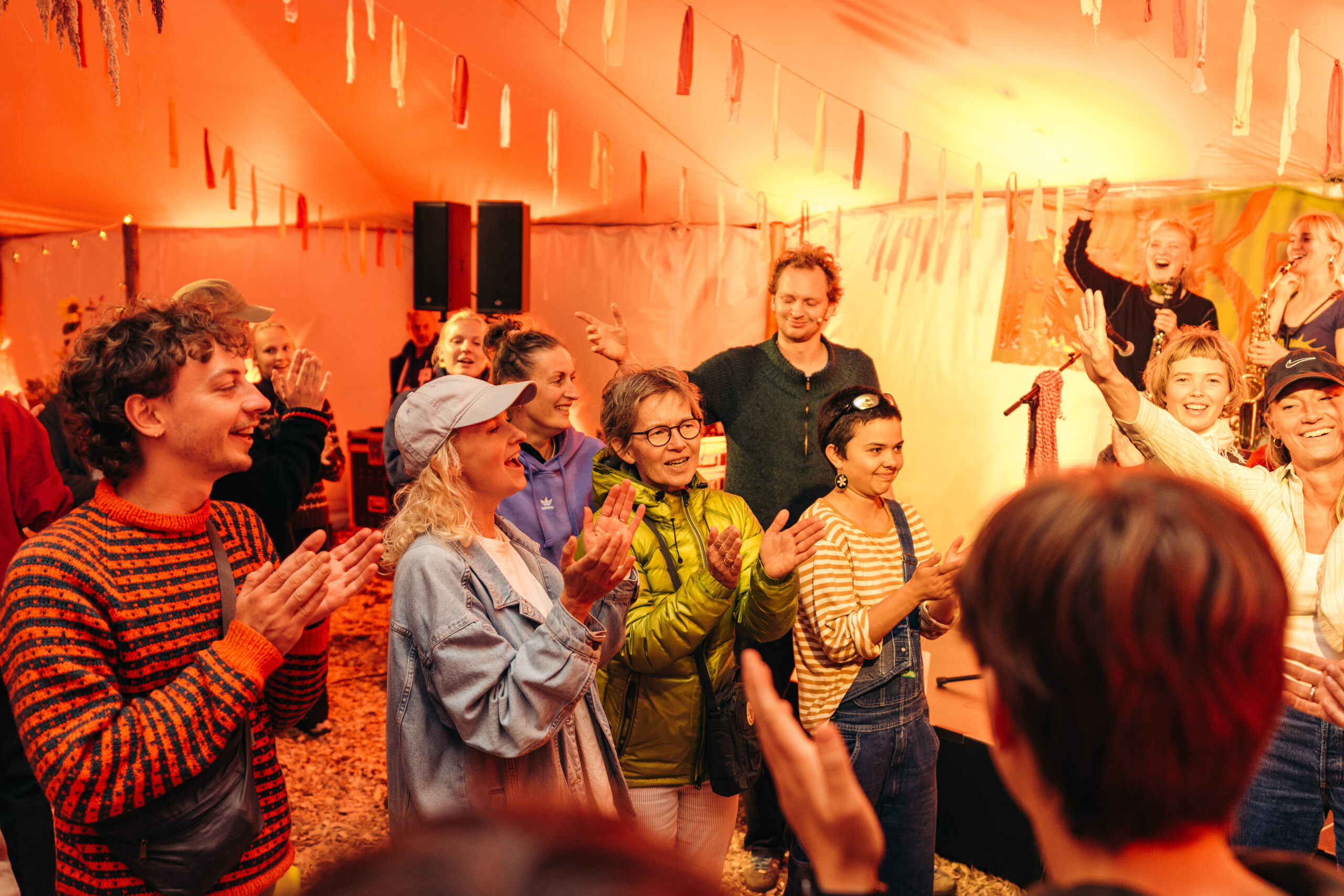 Mennesker griner og klapper sammen i et telt på campen